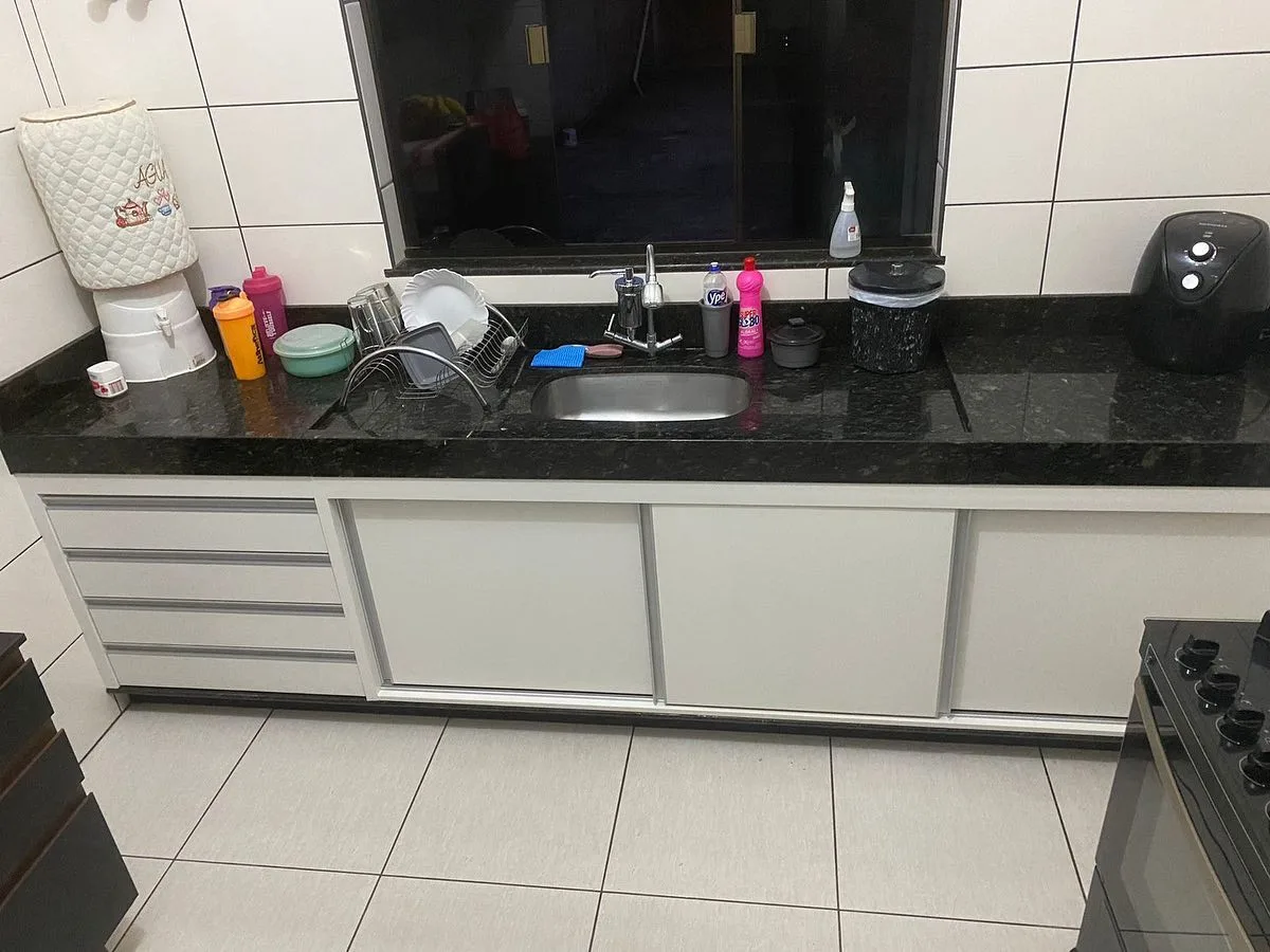 Balcão de pia branco com gaveteiro e portas, sob bancada de granito preto